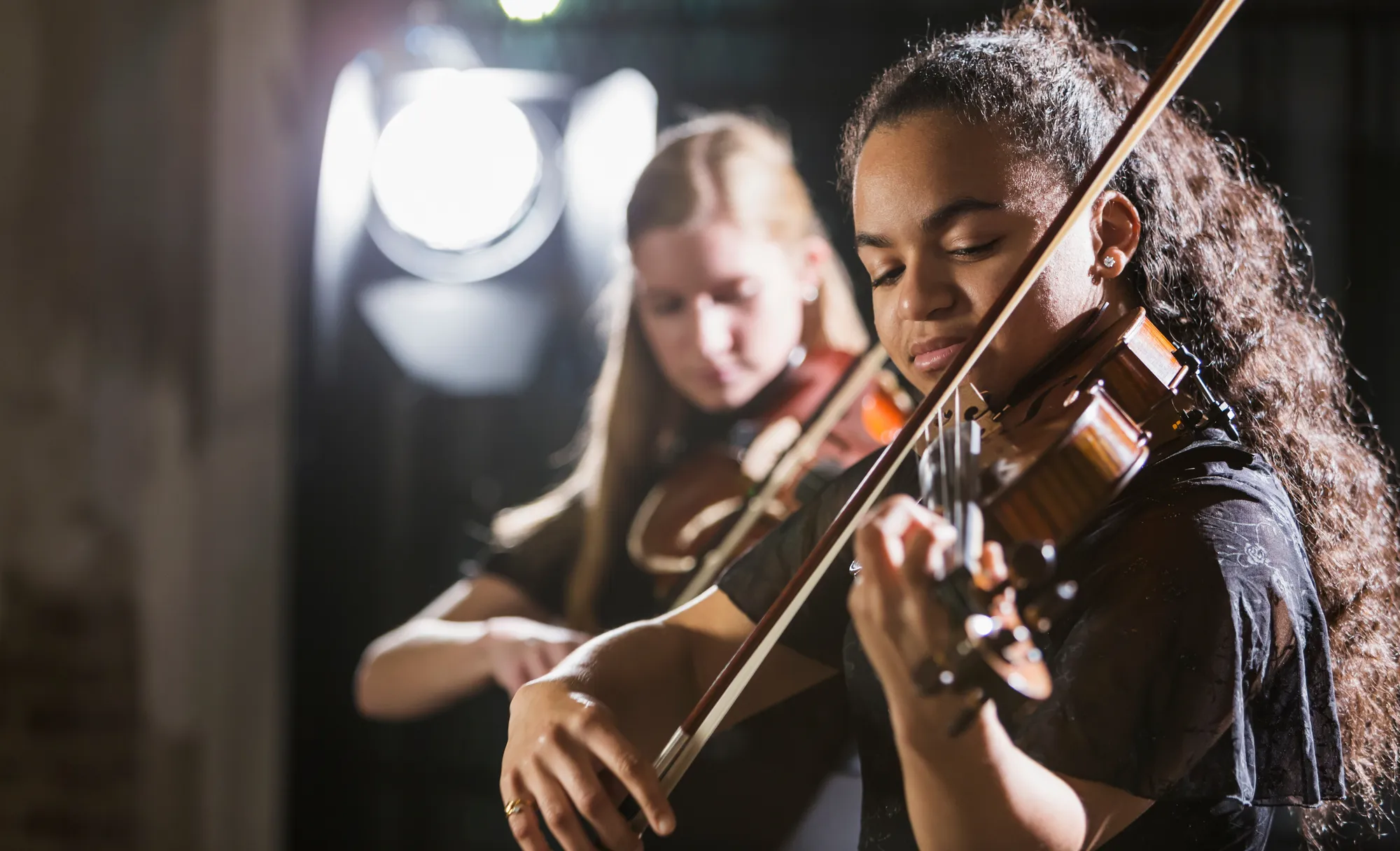 Deux jeunes filles jouant du violon, l'une est au premier plan et l’autre floutée